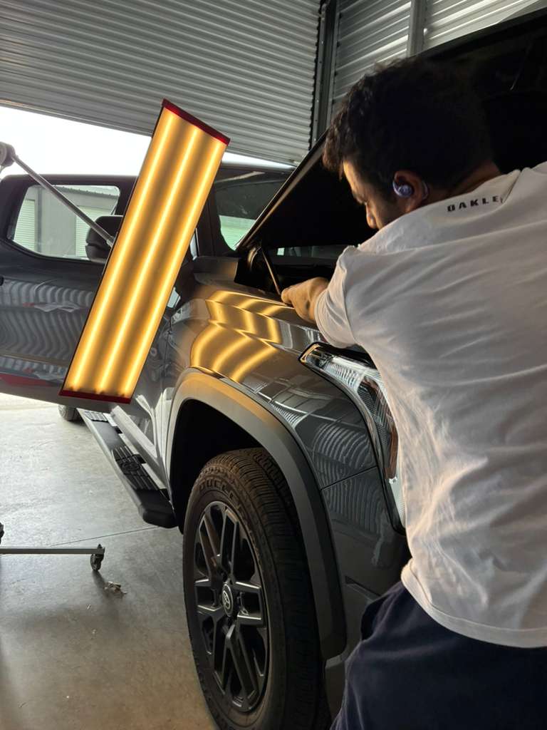 Certified PDR technician using reflection board to repair dent on luxury SUV in Madison WI shop